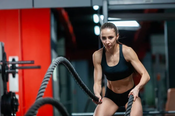 En attraktiv ung muskulös flicka med träningsrep för kamprep motion i ett gym — Stockfoto