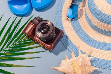 Turkuaz mavi arka plandaki plaj aksesuarları, güneş gözlükleri, mavi parmak arası terlikler, çizgili şapka, kamera, kabuk ve palmiye yaprağı. Uzun zamandır beklenen deniz ve seyahat tatili kavramı. Reklamcılık