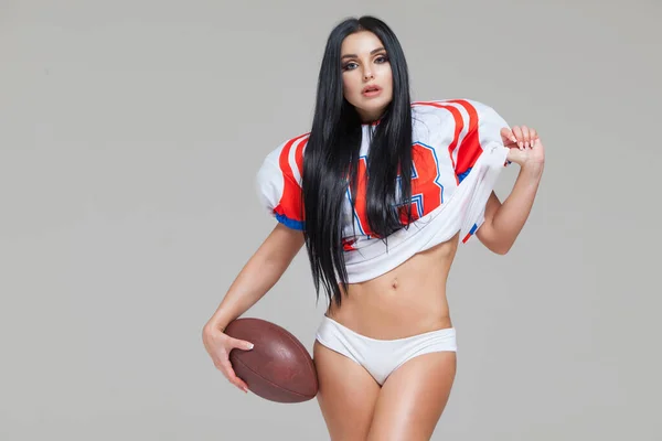 Zdjęcie seksownej atrakcyjnej kobiety amerykańskiej piłkarki nożnej w mundurze i koszulce Jersey, pozującej z piłką odizolowaną na szarym tle — Zdjęcie stockowe