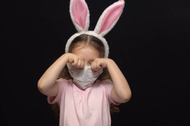 Koronavirüs ve hava kirliliği kavramı. Küçük bir kız koruma için maske takıyor ve Paskalya Tavşanı kostümü giyiyor. Mahvolmuş bir bayram için ağlamak beni endişelendiriyor. Sıkıntılı bir çocuk. Paskalya Toplantısı