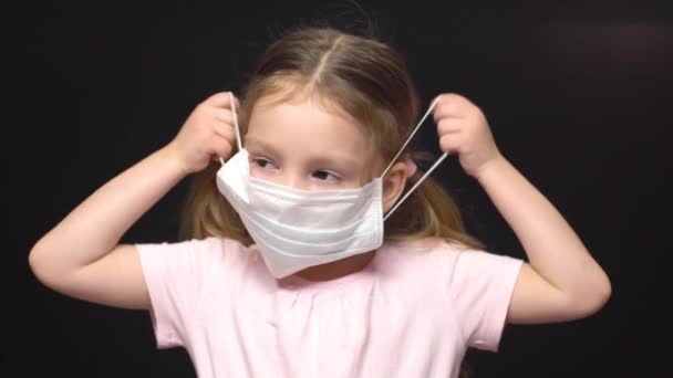 Coronavirus en luchtverontreiniging concept. Een klein meisje draagt een masker ter bescherming. Wuhan coronavirus en epidemische virussymptomen. Ze probeert een beschermend medisch masker op te zetten, maar het werkt niet omdat — Stockvideo