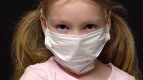 Концепция коронавируса и загрязнения воздуха. Маленькая девочка в маске для защиты. Коронавирус Ухана и симптомы эпидемии вируса. Бедный ребенок машет рукой и поднимает большой палец. Изолированный на черном — стоковое видео