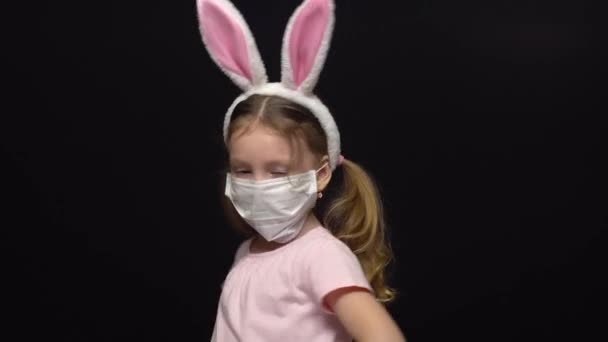 Concetto di coronavirus e inquinamento atmosferico. Una bambina indossa una maschera di protezione e un costume delle orecchie di coniglio pasquale. Preoccupazioni per una vacanza rovinata. Agitando le maniglie e filando. Riunione della — Video Stock