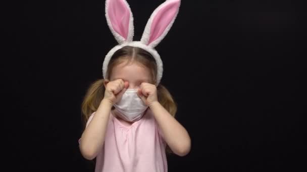 珊瑚病毒和空气污染的概念。一个小女孩戴着面具作为保护，穿着复活节兔子耳朵的服装。担心为一个被毁的假期哭泣。一个苦恼的孩子复活节的会议 — 图库视频影像