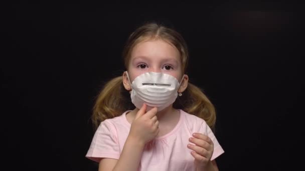 Coronavirus and Air pollution concept. Little girl wearing mask for protect. Wuhan coronavirus and epidemic virus symptoms. Adjusts the mask with his hand. Isolated on a black background — Stock Video