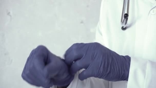 Acercamiento de manos de médico africano, que se pone guantes azules de pie contra una pared de hormigón, y luego toma un par de gafas de seguridad del bolsillo de su bata blanca de laboratorio y las pone en su — Vídeos de Stock