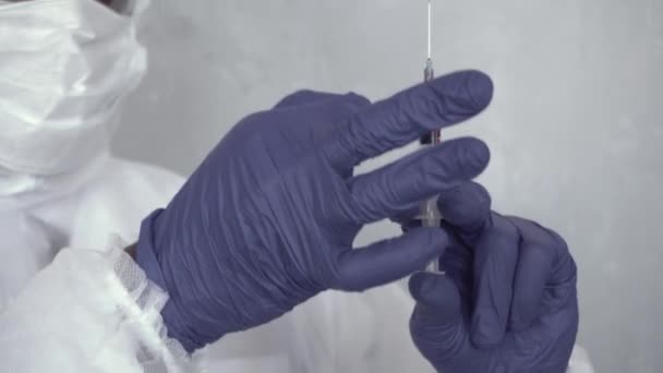 Close-up of a black man in a chemical protection suit holding a blood syringe in his hand, shaking it off, and then looking at the camera. Coronavirus, epidemic, pandemic, COVID-19, flu, cold — Stock Video