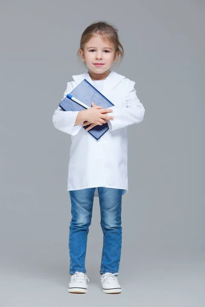 Roztomilé dítě dívka uniformované jako lékař drží lékařské záznamy izolované na šedém pozadí — Stock fotografie