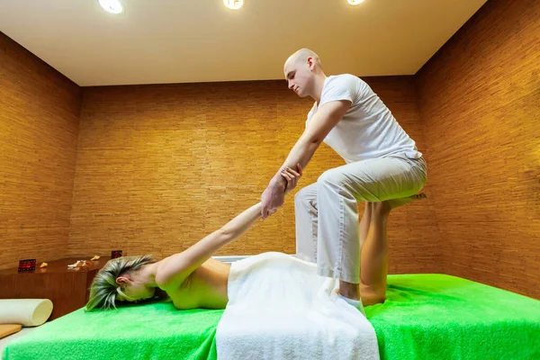 Vue latérale prise sur masseur tire les bras de la femme faisant massage thaïlandais traditionnel sur le corps de la femme dans le salon de spa. Concept de traitement beauté — Photo