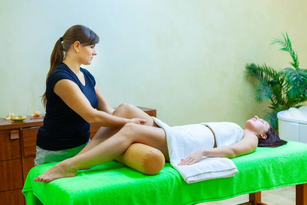 Vista frontal do terapeuta de massagem profissional dando massagem nas pernas da mulher no salão de spa — Fotografia de Stock