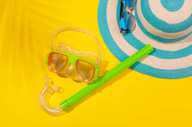 Sarı arka planda plaj aksesuarları, çizgili mavi şapka ve dalış maskesi. Plaj tatili kavramı, deniz turu, sıcak güneşli yaz. Reklam alanı