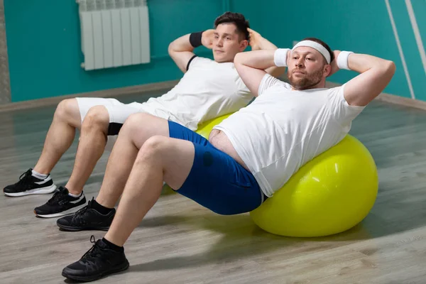 Cansado homem gordo está deitado em um treinamento de bola de fitness durante as aulas de fitness em grupo. Sobrepeso — Fotografia de Stock