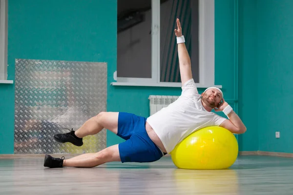 Hombre gordo sonriente está haciendo ejercicios usando la pelota de fitness. Hombre con sobrepeso está contento con el resultado de su entrenamiento en clases de fitness en grupo — Foto de Stock