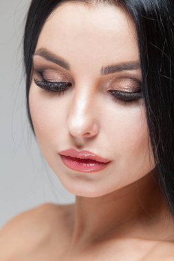 Güzellik makyajlı güzel bir kadın yüzü ve gri arka planda uzun esmer saçlar.