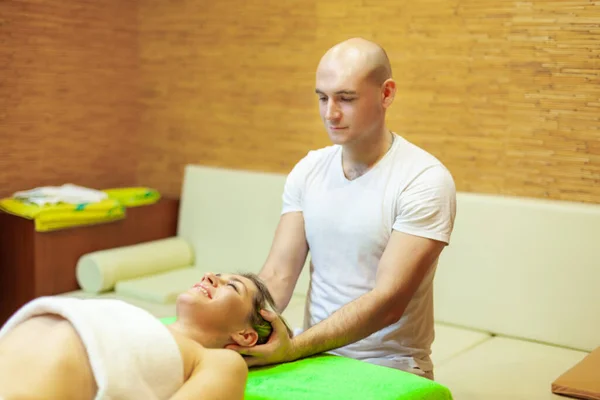 Повна релаксація. Красива молода жінка лежить на спині, а професійний масажист масажує голову — стокове фото