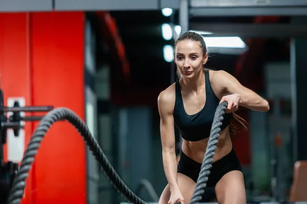 Uma jovem menina muscular atraente usando cordas de treinamento para o exercício de cordas de batalha em um ginásio — Fotografia de Stock
