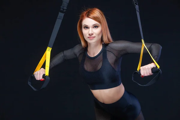 Όμορφη fitness woman κατάρτισης με trx ιμάντες γυμναστικής σε σέξι αθλητικά ρούχα που απομονώνονται σε μαύρο φόντο — Φωτογραφία Αρχείου