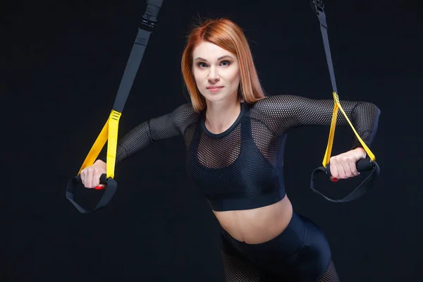 Mooie fitness vrouw training met trx fitness bandjes in sexy sportkleding geïsoleerd op zwarte achtergrond — Stockfoto