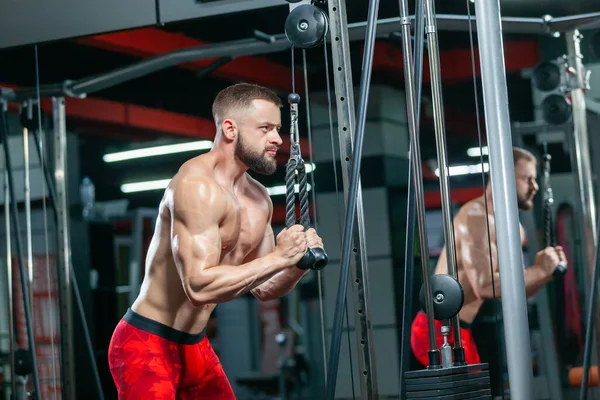 Starker muskulöser Mann trainiert seinen Trizeps mit Sportgeräten in der modernen Turnhalle — Stockfoto