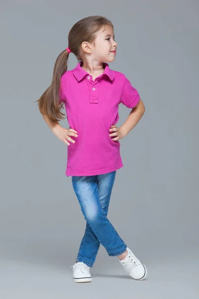 Full length portrait of funny active little girl wearing casual clothes: jeans and pink t-shirt isolated on grey studio background — Stock fotografie