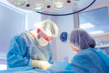 Bir grup cerrah ameliyathanede çalışıyor. İki doktor bir hastaya ameliyat yapıyor.