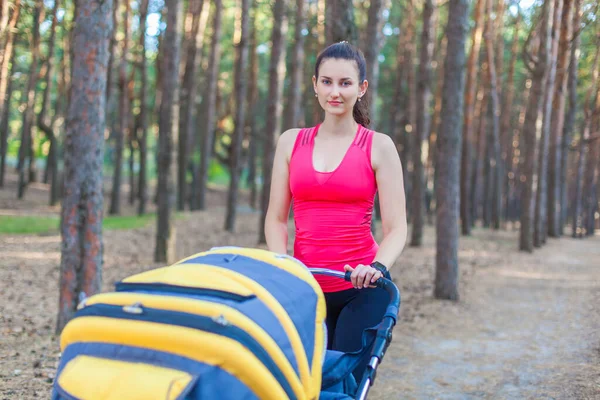 Nature walk with stroller, young active mother in sportswear walking on the forest walkway with her baby in the pram, enjoying fresh air — Stock Photo, Image