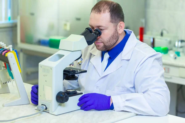 Specialista che cerca attraverso il microscopio effettuando ricerche scientifiche in un laboratorio. Test delle urine. COVID-19. COVID Coronavirus — Foto Stock