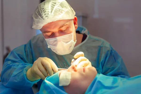 Primer plano de la cara de un paciente que se somete a una blefaroplastia. El cirujano corta el párpado y realiza manipulaciones utilizando instrumentos médicos —  Fotos de Stock