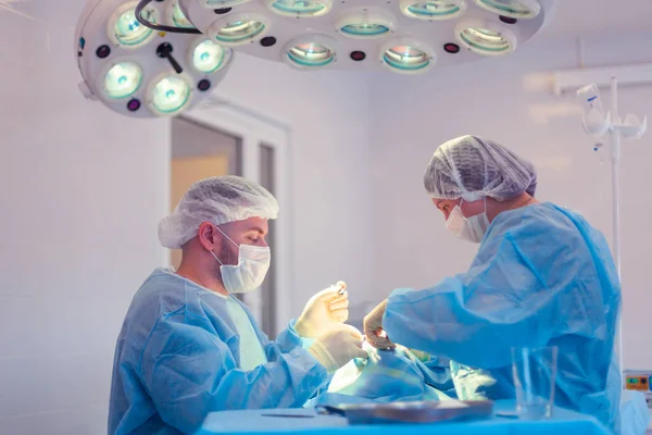 남자 외과의사는 수술실에서 수술을 하고 조수는 환자 상태를 관찰 한다 — 스톡 사진