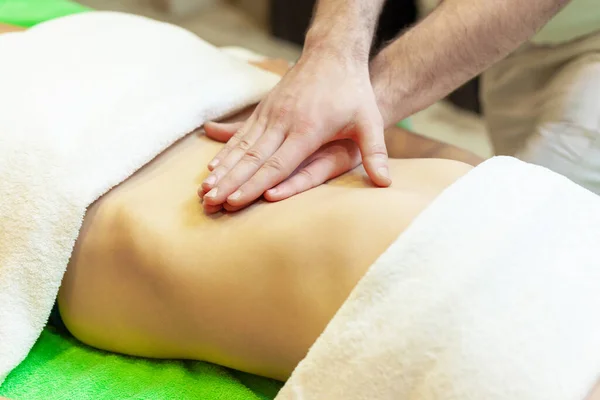 Vista lateral das mãos massagear o abdômen feminino. Terapeuta a pressionar a barriga. Mulher recebendo massagem no salão de spa — Fotografia de Stock