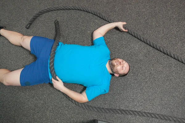 Överviktig man ligger på golvet utmattad efter att ha utfört strid rep motion i gymmet — Stockfoto