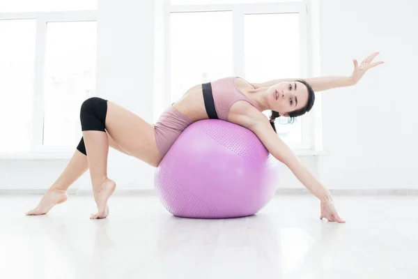 Young slender girl strengthens the back muscles with the help of fitness ball