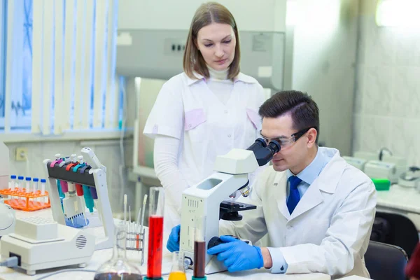 Forskaren forskar i mikroskop i ett medicinskt laboratorium. Vetenskapsman med en assistent. Covid-19. Covid Coronavirus — Stockfoto