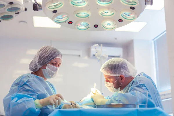 У операційній кімнаті працює група хірургів. Два лікарі проводять операцію на пацієнта — стокове фото