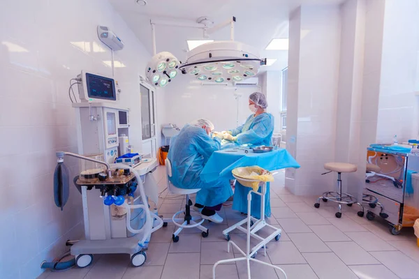 Foto de un monitor de signos vitales y equipo médico junto a dos cirujanos que realizan cirugía en el quirófano —  Fotos de Stock