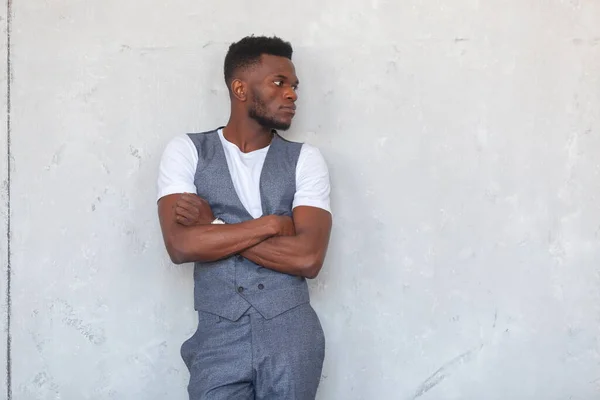 Gri yelek ve pantolonla gri beton bir duvara karşı çapraz kollu poz veren Afrikalı genç yakışıklı bir zenci. — Stok fotoğraf