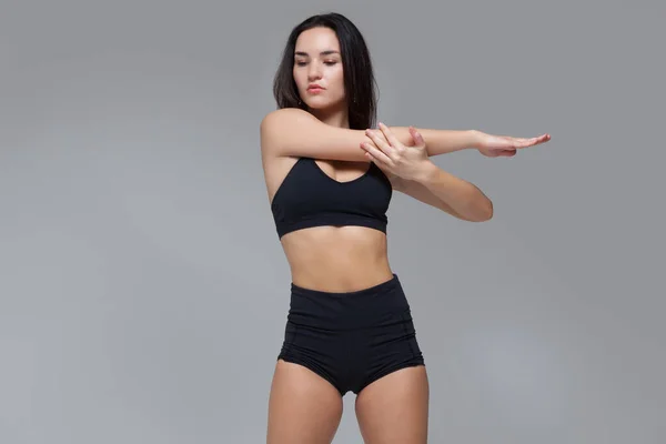 Aantrekkelijke jonge en sexy brunette vrouw met perfect lichaam doet stretching oefening geïsoleerd over grijze achtergrond — Stockfoto