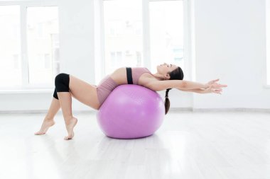 Genç, narin kız spor topu yardımıyla sırt kaslarını güçlendiriyor.