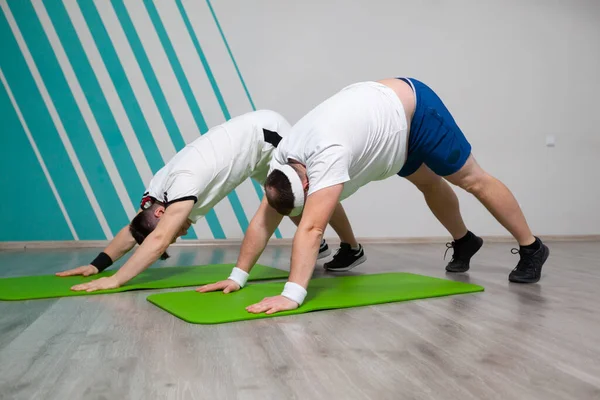 胖男人和他的私人教练正在健身房里努力工作，尽可能多地在垫子上做运动 — 图库照片