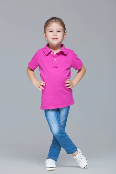 Full length portrait of funny active little girl wearing casual clothes: jeans and pink t-shirt isolated on grey studio background — 스톡 사진