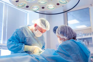 Bir grup cerrah ameliyathanede çalışıyor. İki doktor bir hastaya ameliyat yapıyor.