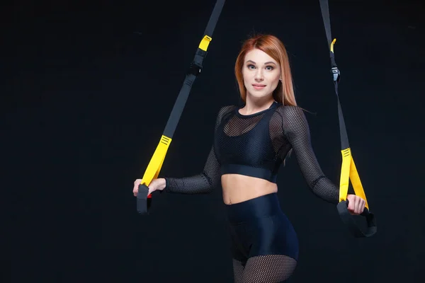 Mooie fitness vrouw training met trx fitness bandjes in sexy sportkleding geïsoleerd op zwarte achtergrond — Stockfoto