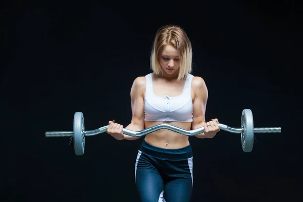 Retrato de cerca de una chica joven musculosa posando con la barra rizada en el gimnasio aislado sobre un fondo negro —  Fotos de Stock