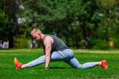 Genç kaslı adam yoga yapıyor ve açık havada bir yaz parkında esniyor.