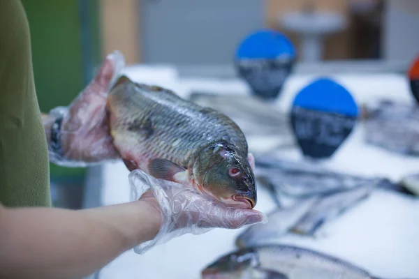 Joven atleta masculino en camiseta verde y guantes sostiene pescado congelado eligiendo comida en una tienda de comestibles — Foto de Stock