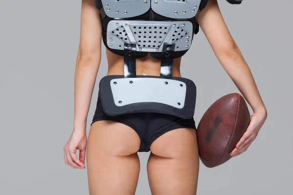 Jong sportief brunette dragen sexy uniform van American football speler poseren met bal kijken naar camera geïsoleerd op grijze achtergrond — Stockfoto