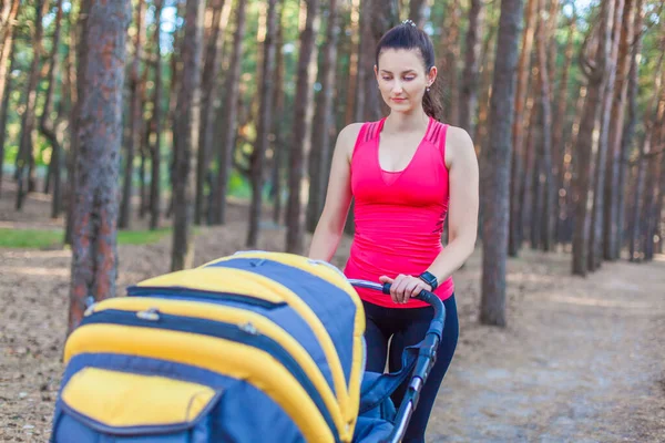 Nature walk with stroller, young active mother in sportswear walking on the forest walkway with her baby in the pram, enjoying fresh air — Stock Photo, Image