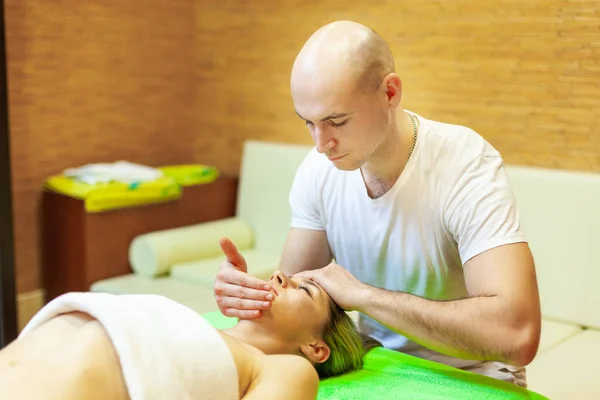 Slappna av. Vacker ung kvinna ligger på rygg medan professionell massage terapeut massera hennes ansikte — Stockfoto