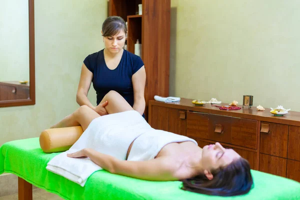 Front view of professional massage therapist giving massage on woman legs in the spa salon — Stock Photo, Image