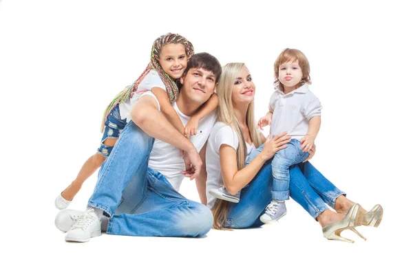 Padres felices con un hijo y una hija en camisetas blancas y vaqueros azules se divierten juntos posando sentados en el suelo aislados sobre fondo blanco — Foto de Stock